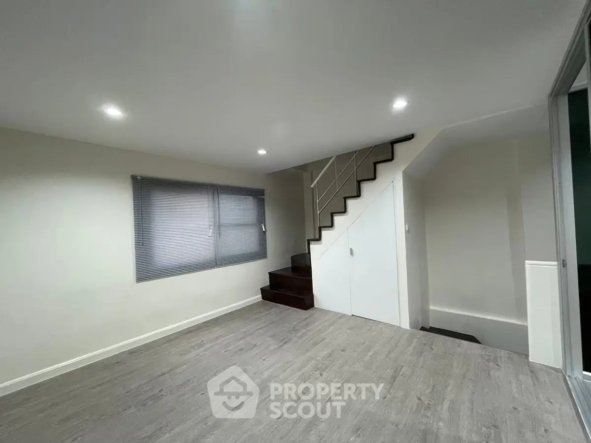 Spacious modern living room with staircase and large window, perfect for family gatherings.