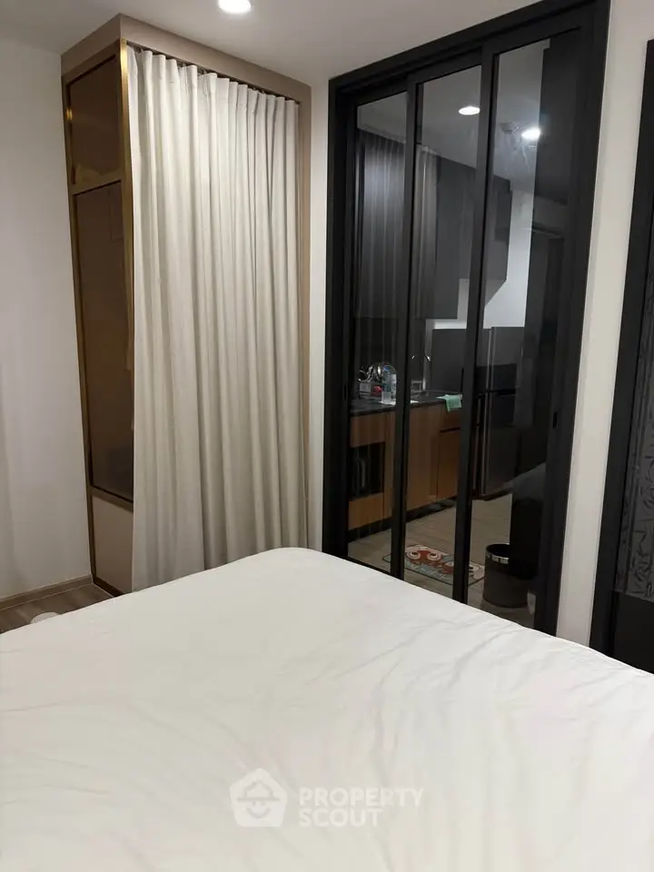 Modern bedroom with glass partition and view into sleek kitchen area.