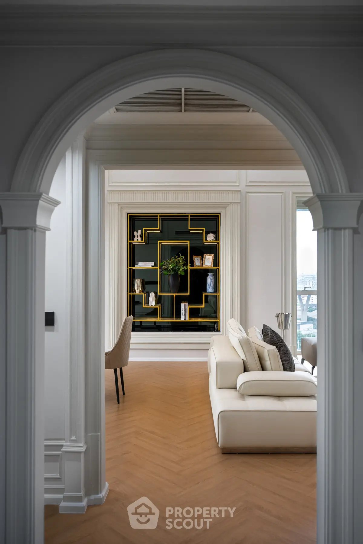 Elegant living room with modern decor and stylish bookshelf through an arched doorway.