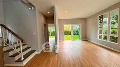 Spacious open living room with large windows and garden view, featuring elegant wooden flooring and modern design.