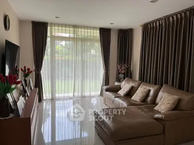 Spacious living room with elegant leather sofa and large window overlooking garden