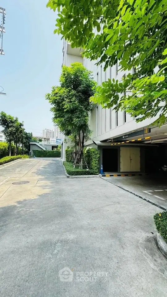 Modern building with lush greenery and spacious parking area under clear blue sky.