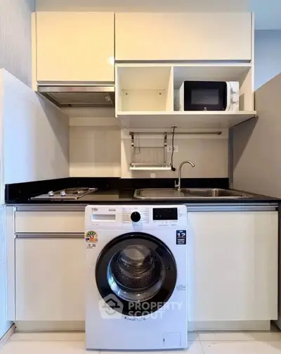 Modern kitchen with washing machine, microwave, and sleek cabinetry in compact layout.
