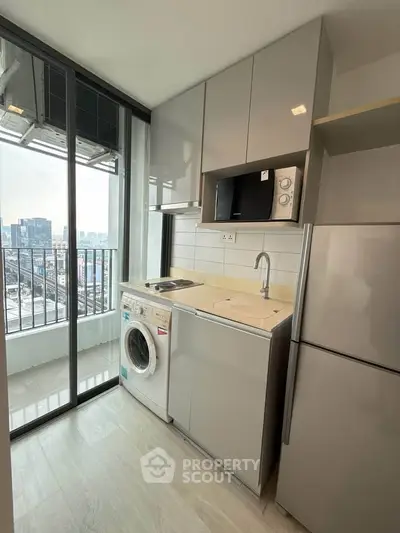 Modern compact kitchen with balcony view, featuring sleek appliances and stylish cabinetry.