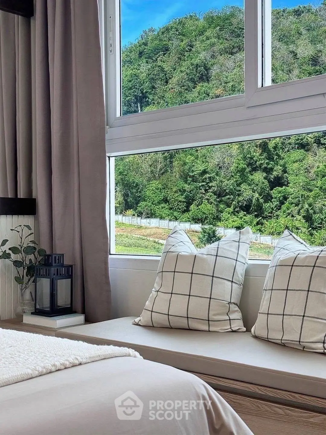 Cozy bedroom with large window offering stunning green view, plush pillows, and elegant decor.