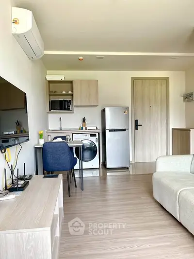 Modern living room with compact kitchen, washing machine, and sleek appliances in a cozy apartment.