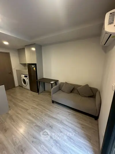 Modern compact living room with sofa, washing machine, and sleek flooring.