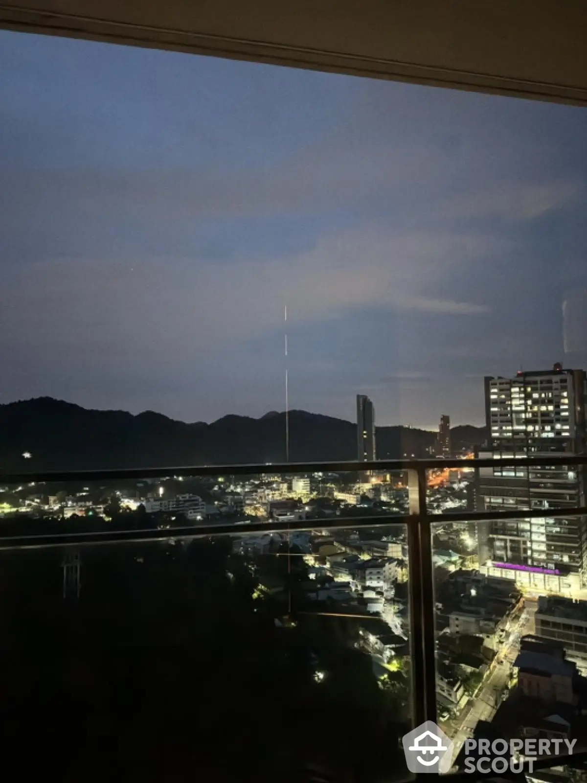 Stunning cityscape view from high-rise balcony at dusk with mountains in the background.