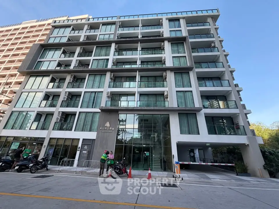 Modern multi-story apartment building with glass balconies and street view.