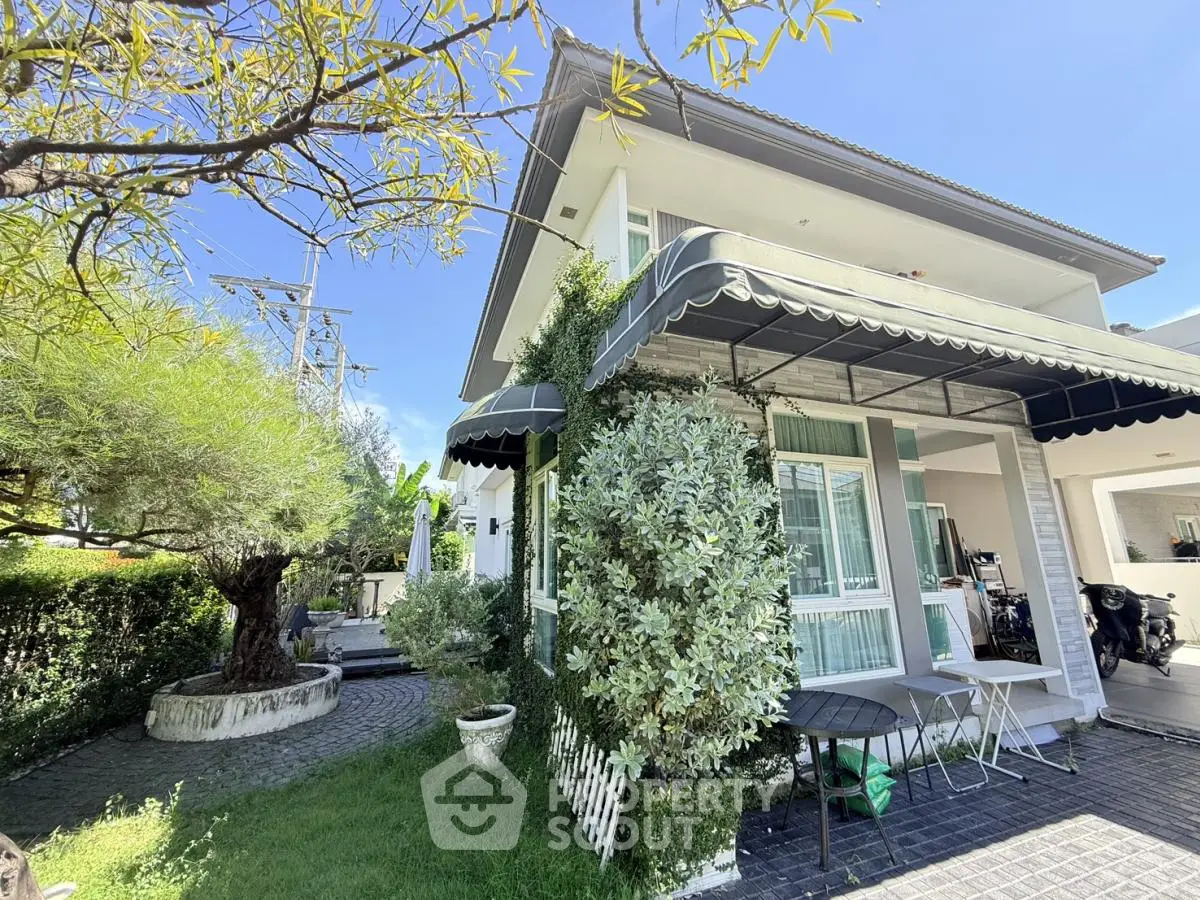 Charming two-story house with lush garden and outdoor seating area, perfect for family living.