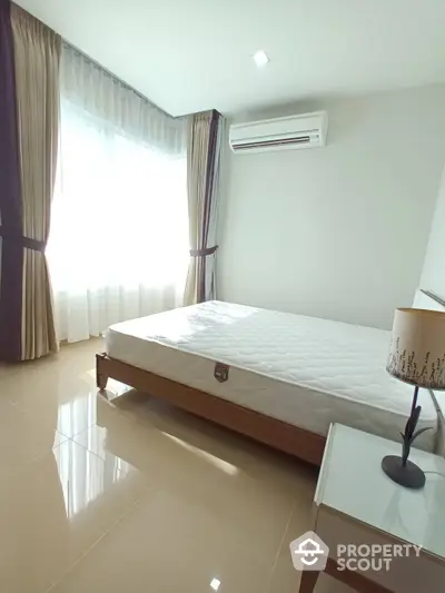 Spacious and well-lit bedroom with glossy tiled flooring, large windows draped with elegant curtains, and modern air conditioning unit.