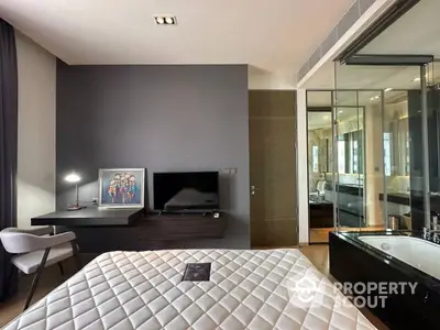 Modern bedroom with sleek design, featuring a luxurious bed, flat-screen TV, and an elegant glass partition leading to an en-suite bathroom.