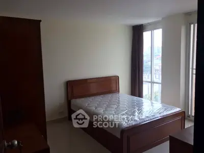 Spacious bedroom with large window and wooden bed frame, offering natural light and a cozy atmosphere.
