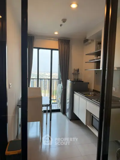 Modern kitchen with open layout and city view from balcony, featuring sleek appliances and dining area.