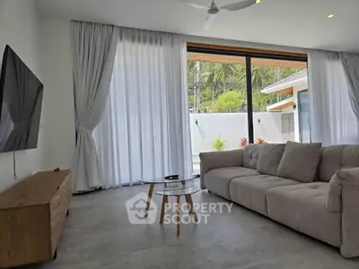 Spacious modern living room with large windows and pool view, featuring a cozy sofa and sleek TV setup.