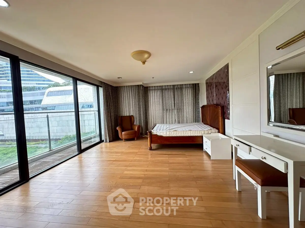 Spacious bedroom with large windows and balcony access, featuring elegant wooden flooring and modern furnishings.