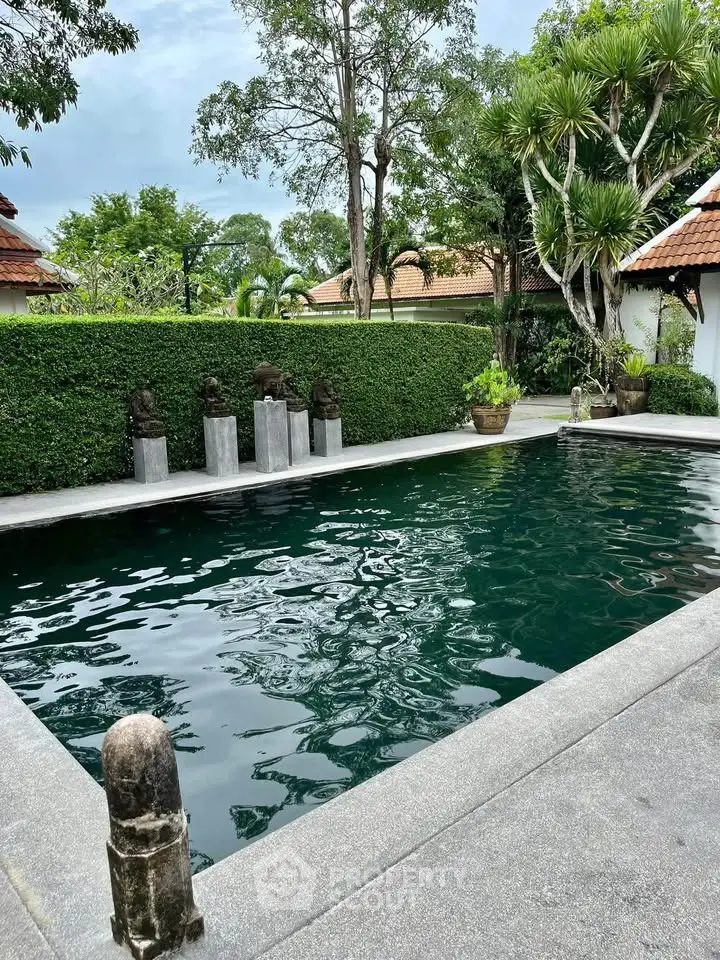 Luxurious outdoor pool surrounded by lush greenery and elegant sculptures in a serene setting.
