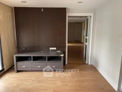 Spacious living room with elegant wooden flooring and a modern entertainment unit, leading to a well-lit corridor.