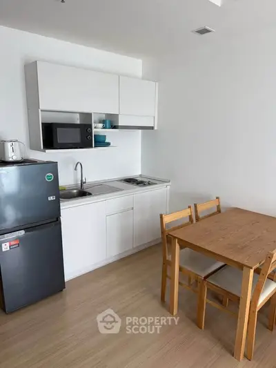 Modern compact kitchen with dining area, featuring sleek cabinetry and wooden furniture.