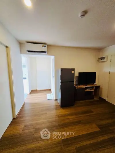 Modern living room with wooden flooring, air conditioning, and compact entertainment setup.