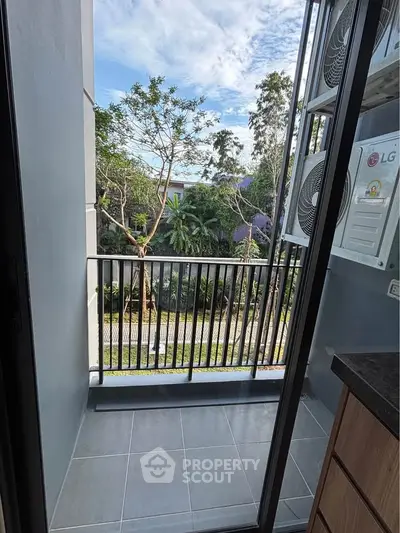 Charming balcony with lush garden view and modern air conditioning units, perfect for relaxation.