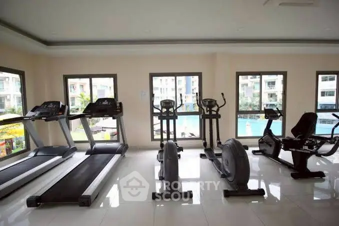 Modern gym with cardio equipment and pool view in luxury apartment complex.