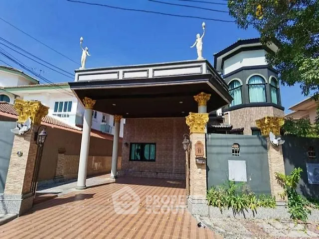 Luxurious entrance of a grand estate with elegant statues and spacious driveway.