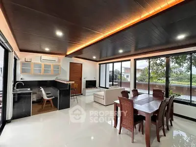 Spacious modern living room with open kitchen and dining area, featuring large windows and elegant ceiling lighting.