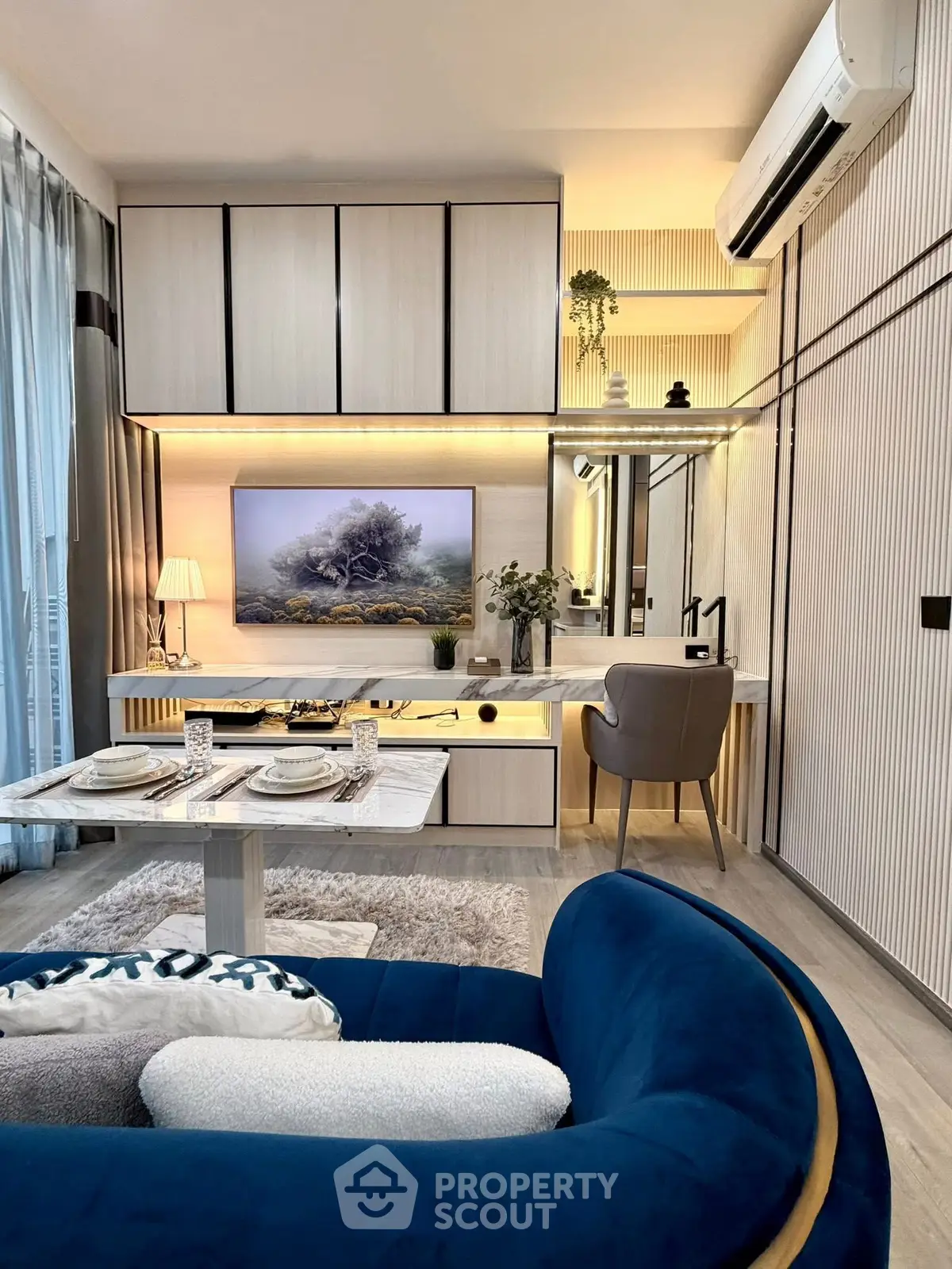 Stylish modern living room with elegant decor and open kitchen layout, featuring a cozy blue sofa and chic dining area.