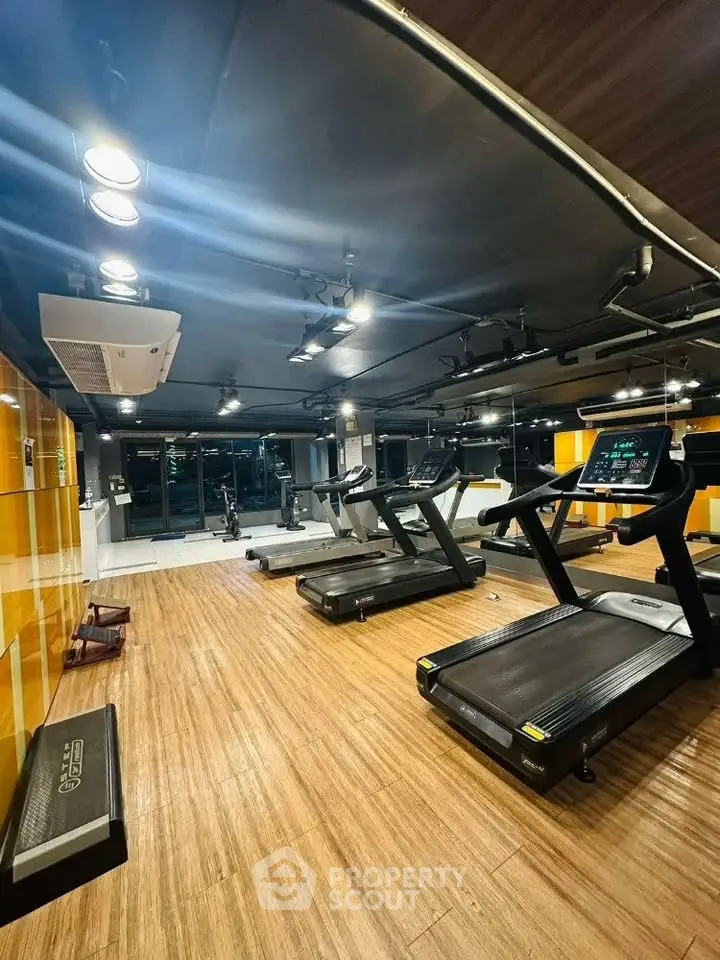 Modern gym with state-of-the-art treadmills and wooden flooring in a luxury apartment complex.