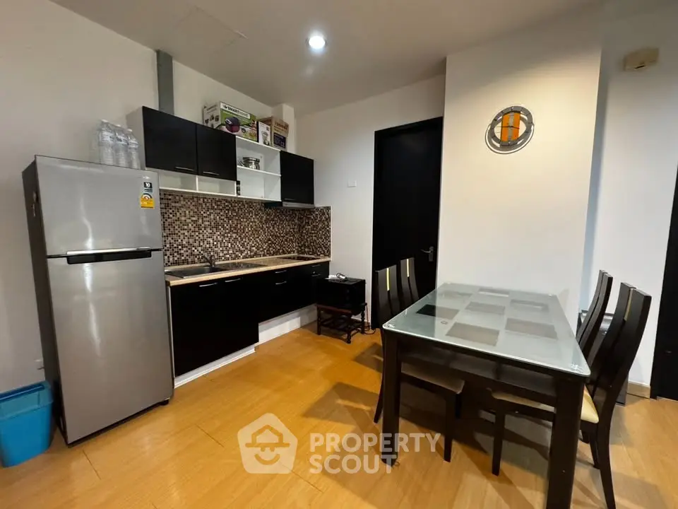 Modern kitchen with sleek black cabinets and dining area in stylish apartment.