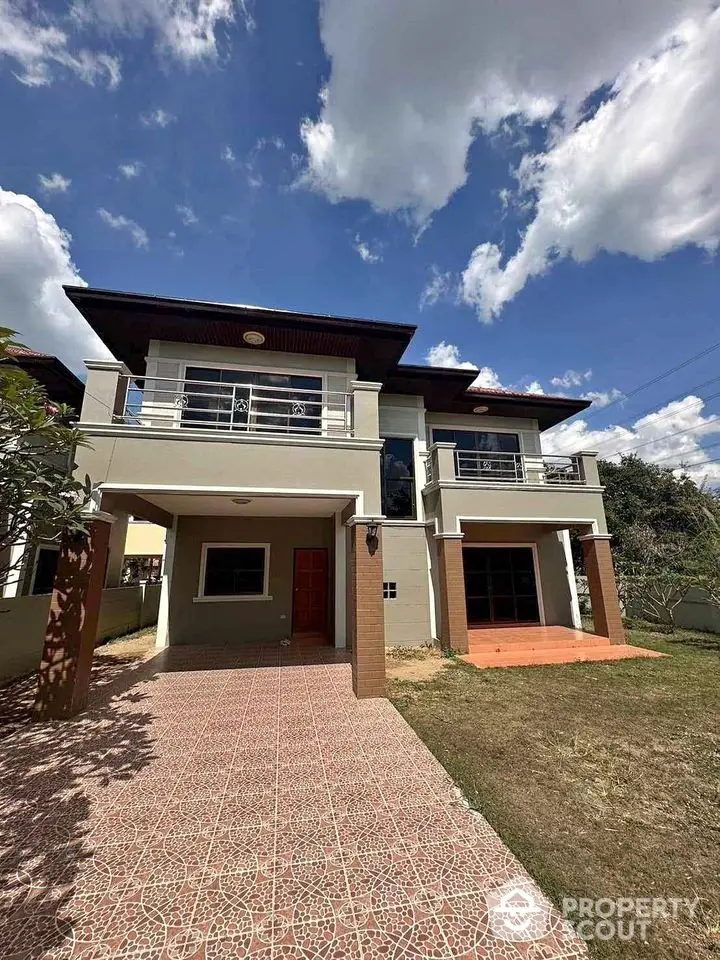 Stunning two-story house with spacious balcony and beautiful garden under clear blue sky.