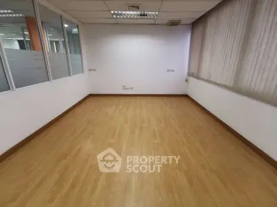 Spacious empty office room with wooden flooring and large windows, ideal for customization.