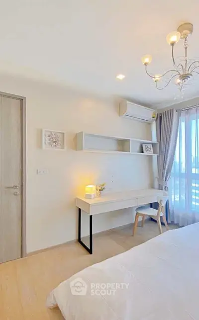 Bright and airy bedroom with modern decor and natural light, featuring a stylish desk and elegant chandelier.
