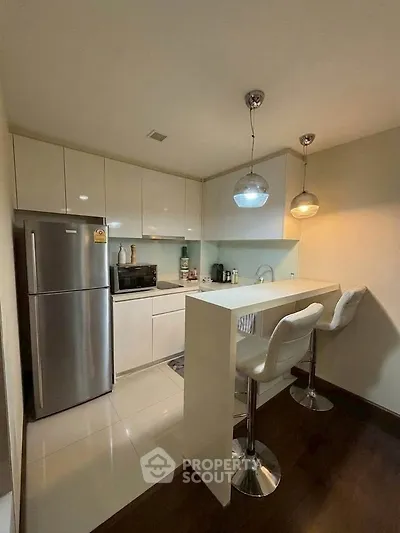 Modern kitchen with sleek white cabinets and breakfast bar, featuring stainless steel appliances and stylish lighting.
