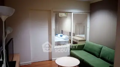 Cozy living room with green sofa and view into bedroom through glass partition.