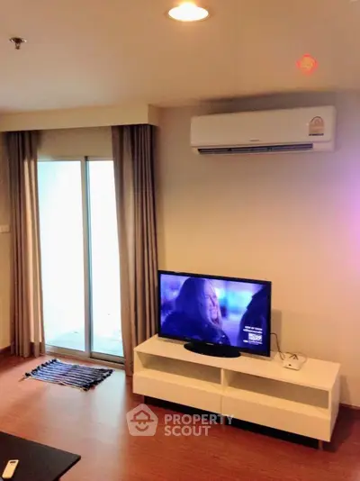 Modern living room with TV and air conditioning, featuring sleek wooden flooring and a sliding glass door.