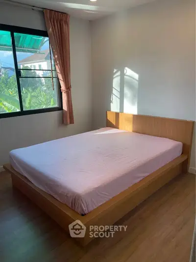 Cozy bedroom with natural light and wooden flooring, featuring a comfortable bed and large window with garden view.