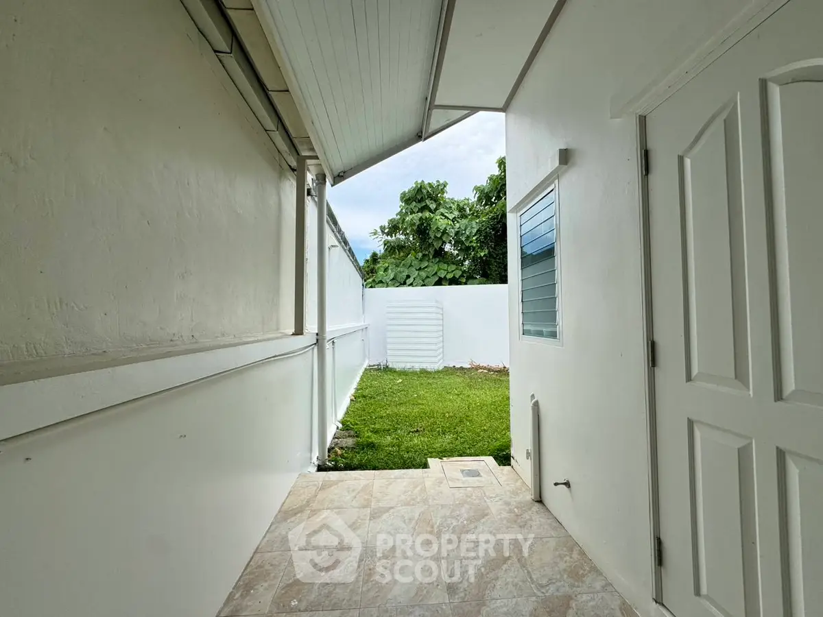 Charming outdoor corridor leading to a lush green garden, perfect for relaxation and outdoor activities.