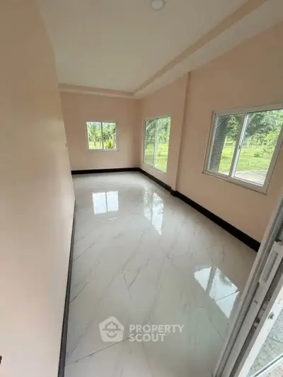 Spacious empty room with large windows and glossy tiled floor, offering serene garden views.