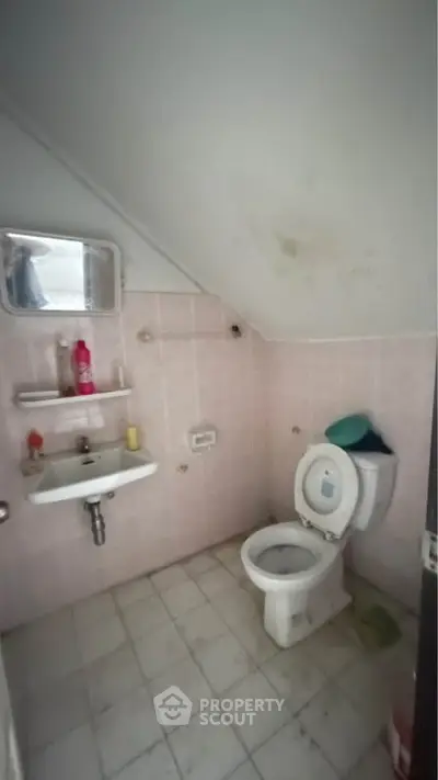 Compact bathroom with sloped ceiling and basic fixtures in need of renovation.