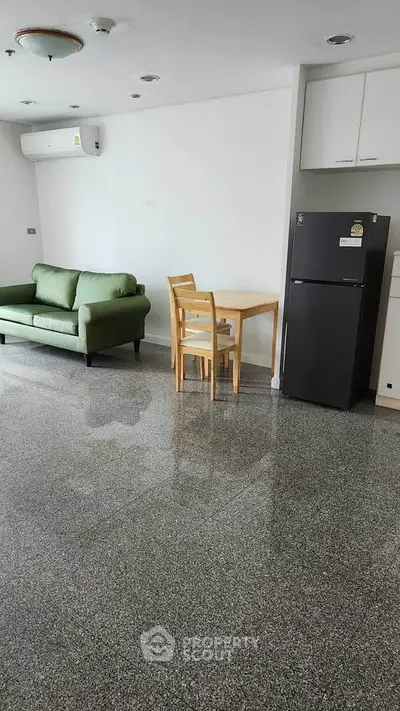 Modern apartment interior with sleek kitchen and cozy living area featuring a green sofa and dining set.