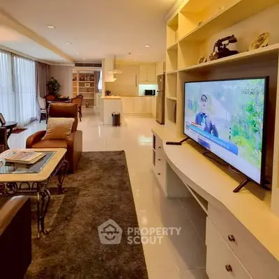Spacious living room with modern decor and large TV, open layout to kitchen area.