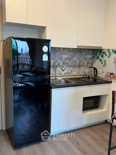 Modern kitchen with sleek black fridge, built-in oven, and stylish backsplash in a compact layout.