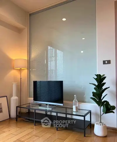 Modern living room with sleek TV stand, stylish lamp, and potted plant on wooden floor.