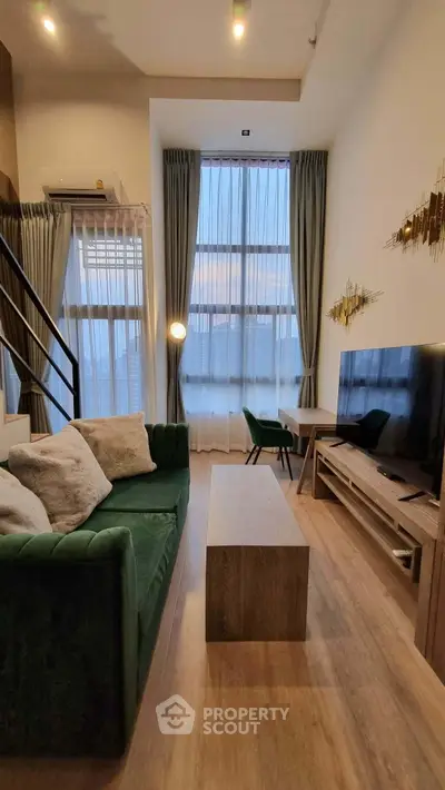 Modern living room with high ceilings, stylish green sofa, and large windows for natural light.