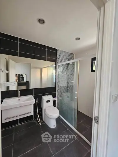 Modern bathroom with sleek design, featuring a glass shower and stylish black tiles.