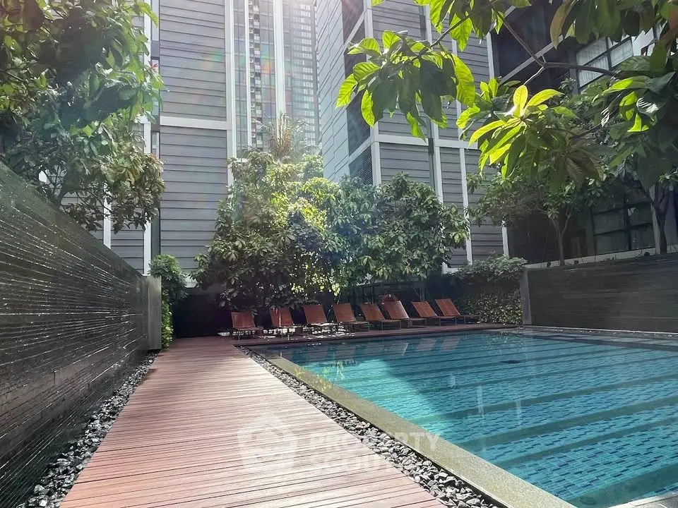 Luxurious outdoor pool area with sun loungers and lush greenery in modern residential complex.