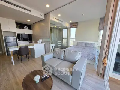 Modern open-plan living room with kitchen and bedroom, featuring sleek furniture and large windows.