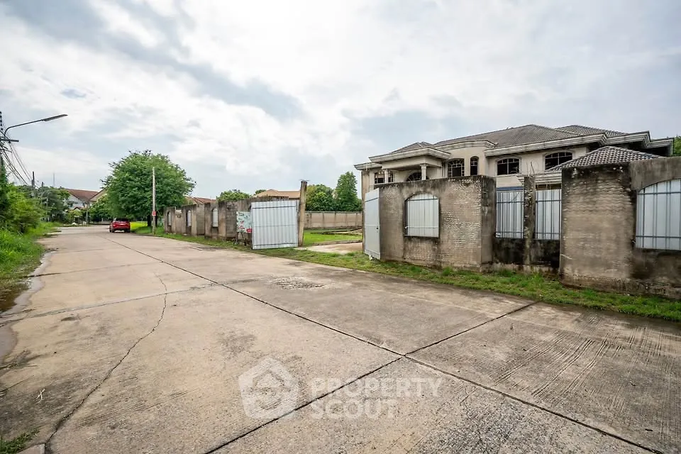 Spacious suburban street view with large gated property and lush greenery.
